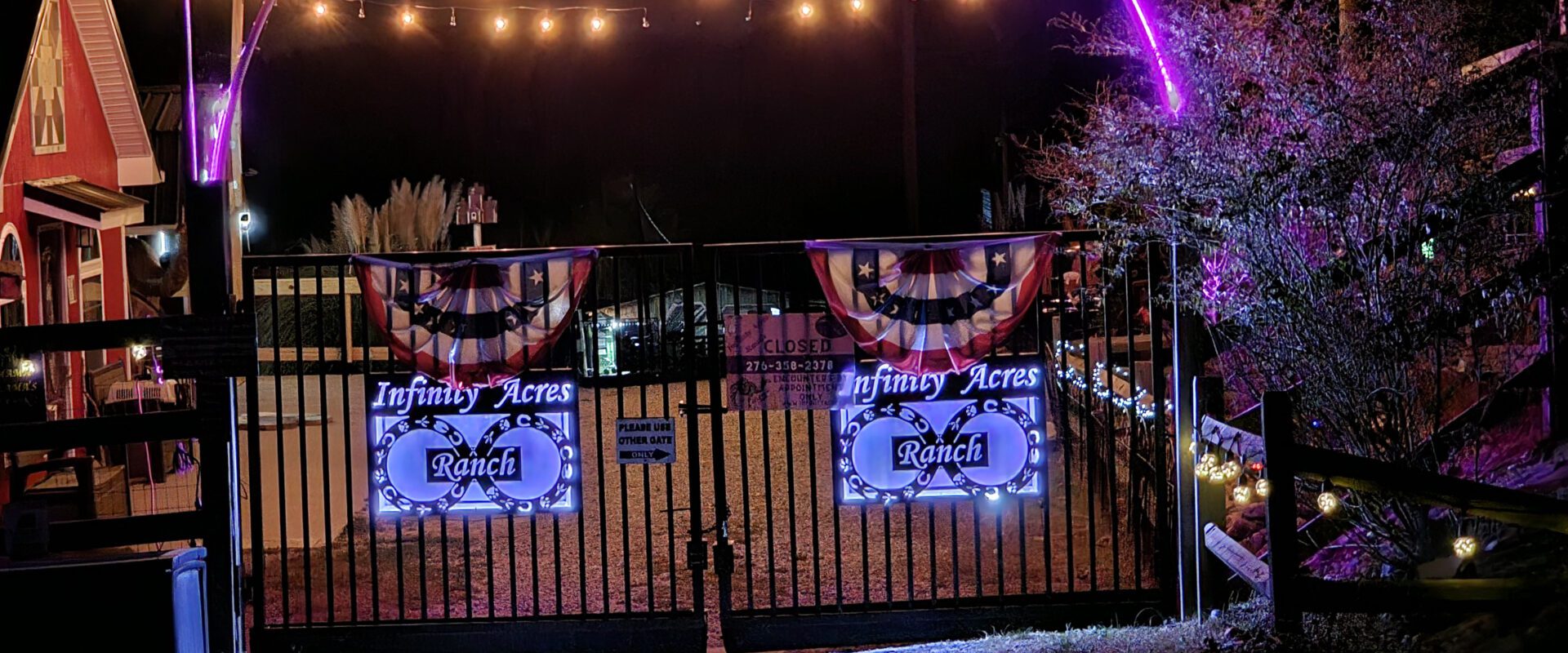 Outdoor evening event with banners and string lights at a fenced area.
