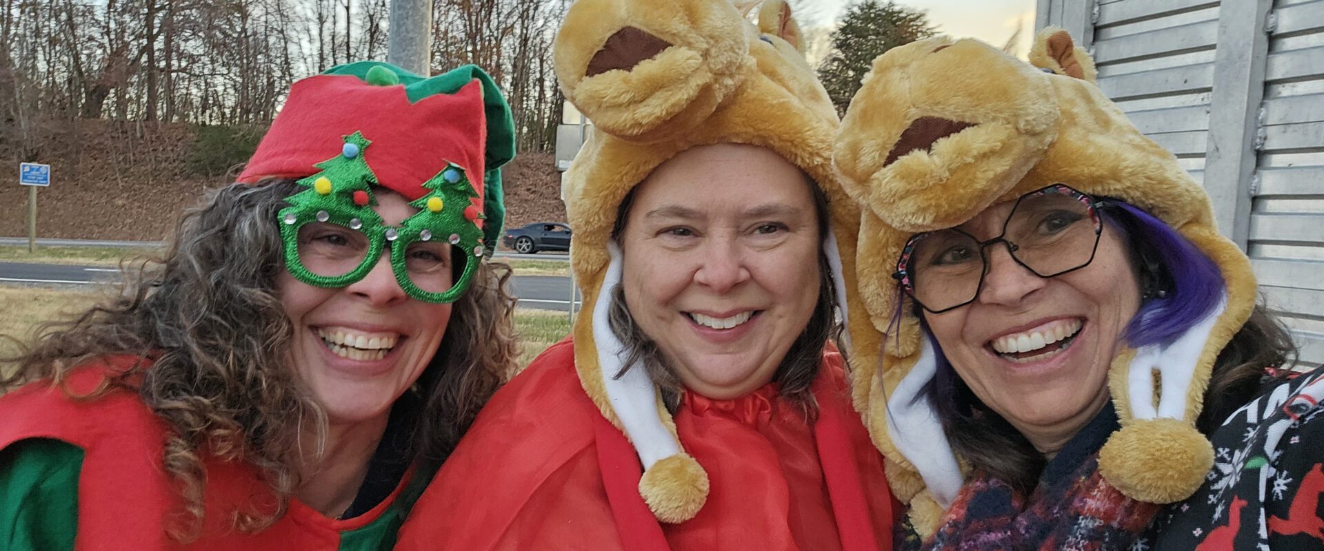 Three people wearing festive holiday costumes and smiling outdoors.