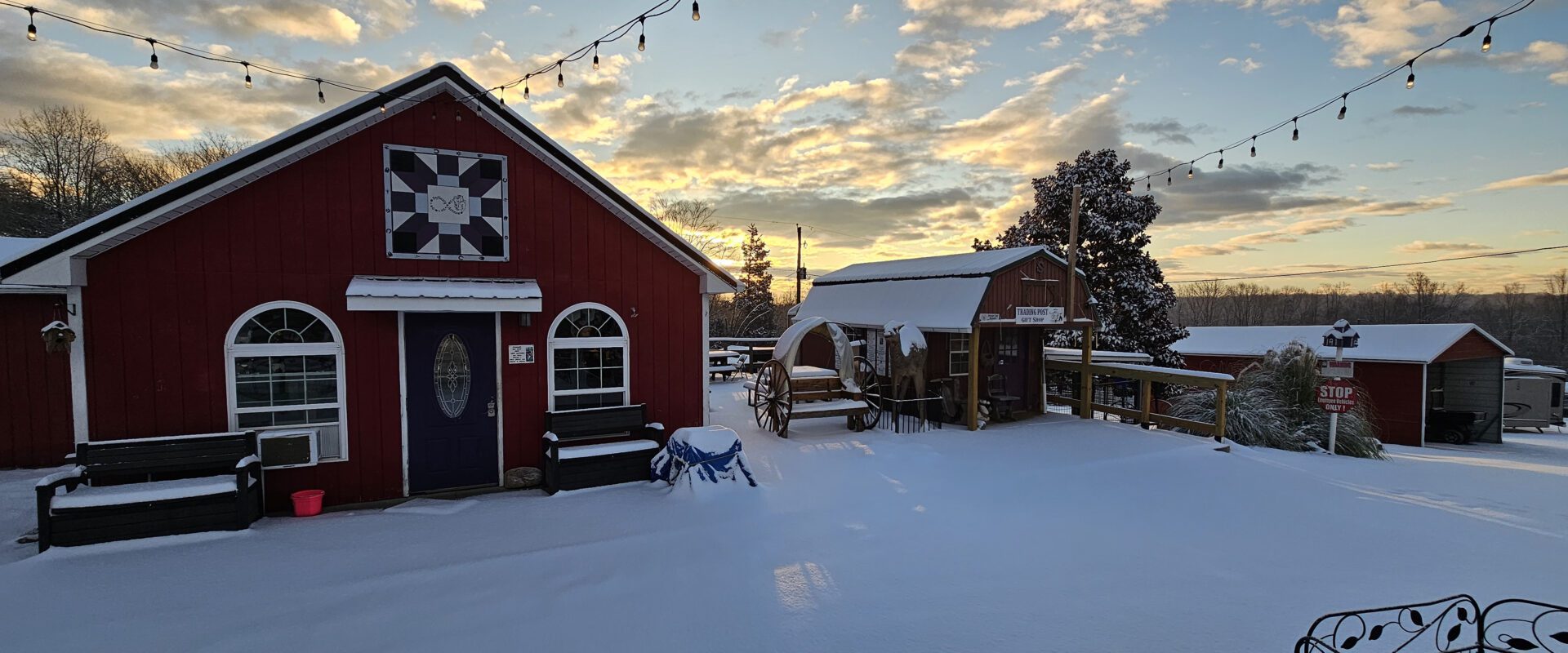 Snow-covered barn and horse statue during a colorful sunset.