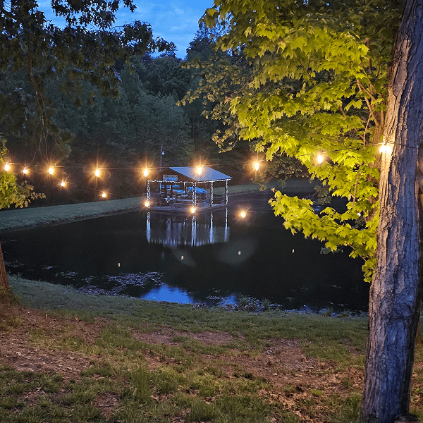 A gazebo lit with string lights on a lake at dusk.