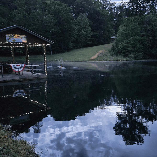 A serene lake reflecting the sky and surrounded by forest, with a small dock and boat.