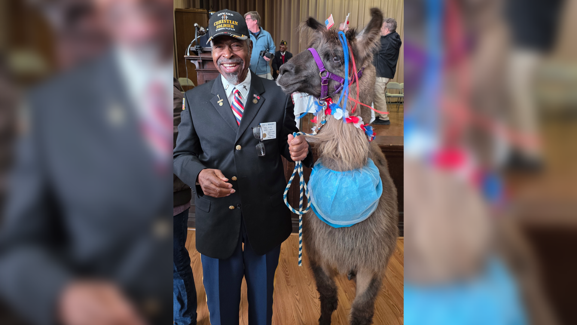 Man in suit holding a decorated llama indoors.
