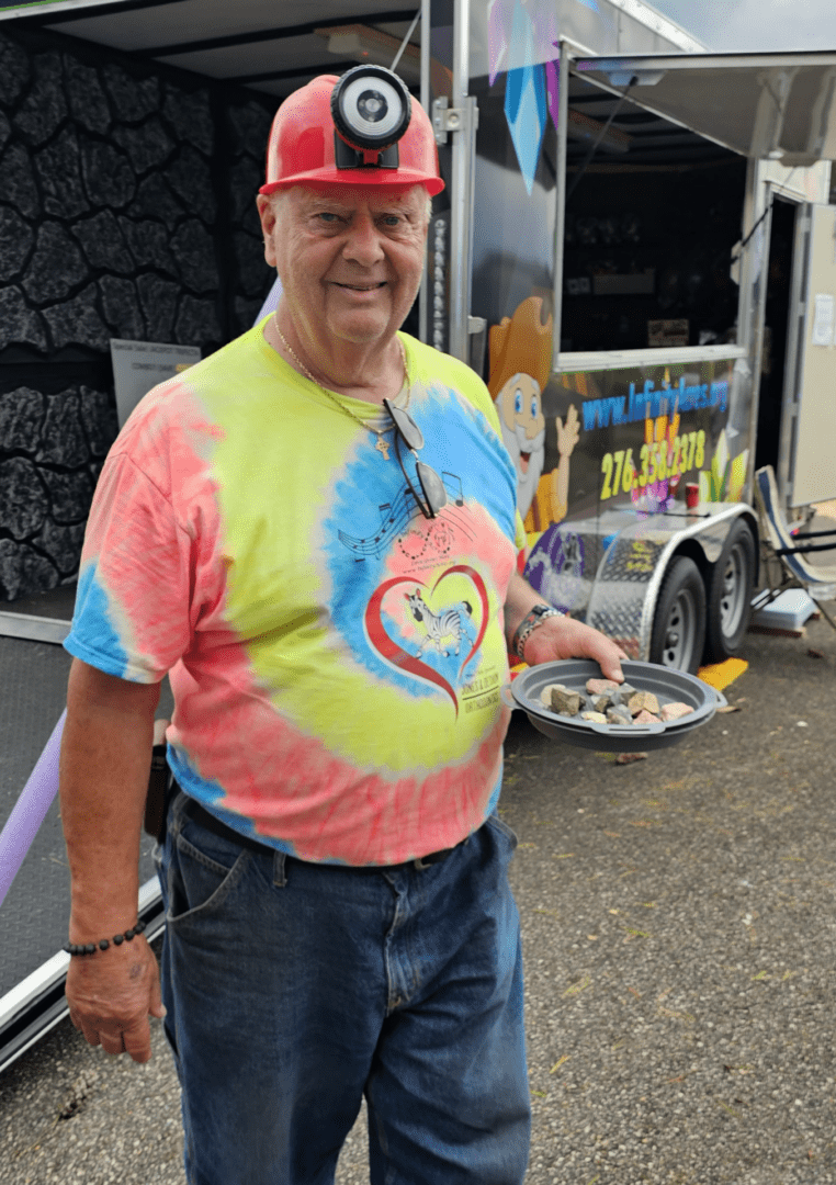 Smiling man in a colorful tie-dye shirt and red cap holding a plate of food.