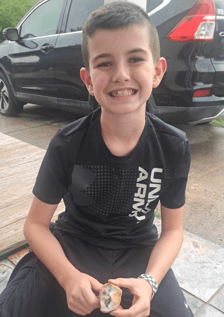 Smiling boy sitting on the floor with a black car behind him.